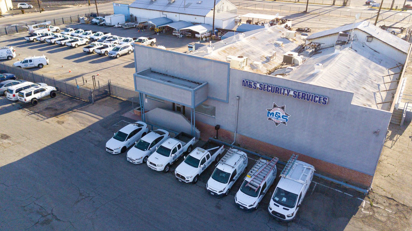 Aerial view of the M&S Security Services building at 2900 L Street, Bakersfield, with the white patrol fleet parked outside